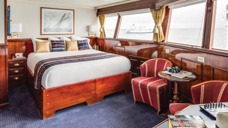 Large bed, desk, small table, two chairs and large windows of cabin aboard National Geographic Islander expedition ship in Galapagos Islands