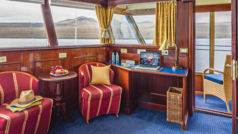 Cabin interior with desk, table, two chairs and private balcony aboard National Geographic Islander in Galapagos Islands