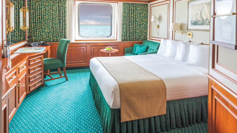 Category 3 cabin with large bed, corner armchair, desk, chair, small table and large window aboard National Geographic Orion expedition ship