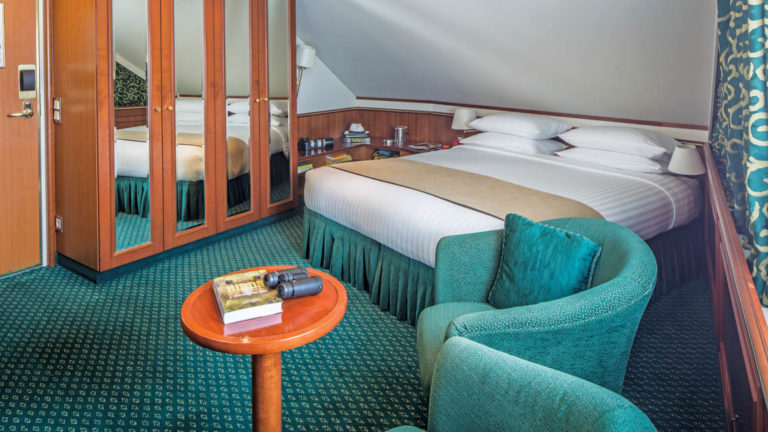 Category 3 cabin with large bed, closet, two armchairs and small table aboard National Geographic Orion expedition ship