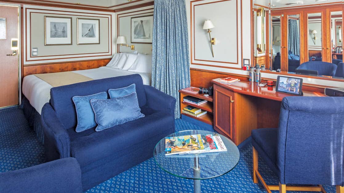 Category 4 cabin with large bed, couch, coffee table, desk and two chairs aboard National Geographic Orion expedition ship