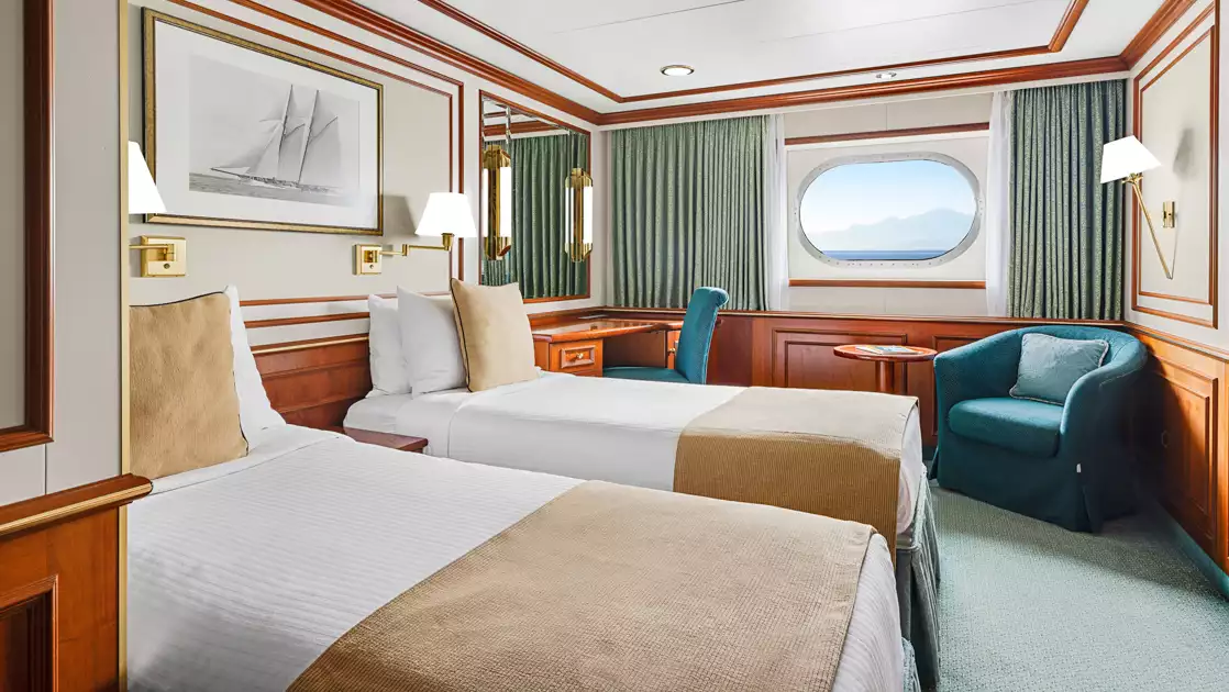 Category 1 cabin on Nat Geo Orion ship with 2 twin beds in white & beige, seating area & shared small window.