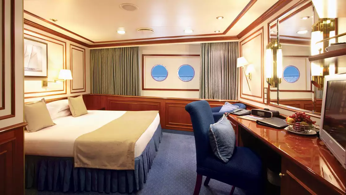 Category 1 Solo cabin on Nat Geo Orion ship with double bed in white & beige, desk & 2 portholes.