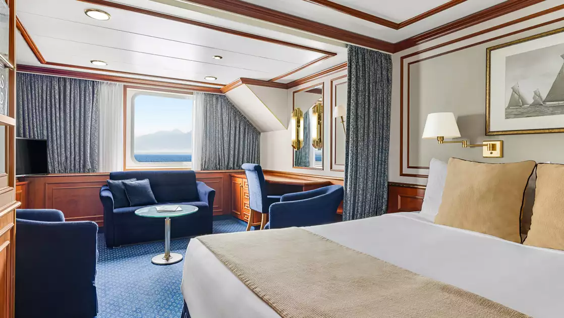 Category 4 cabin on Nat Geo Orion ship with double bed in white & beige, curtain to seating area & large window.