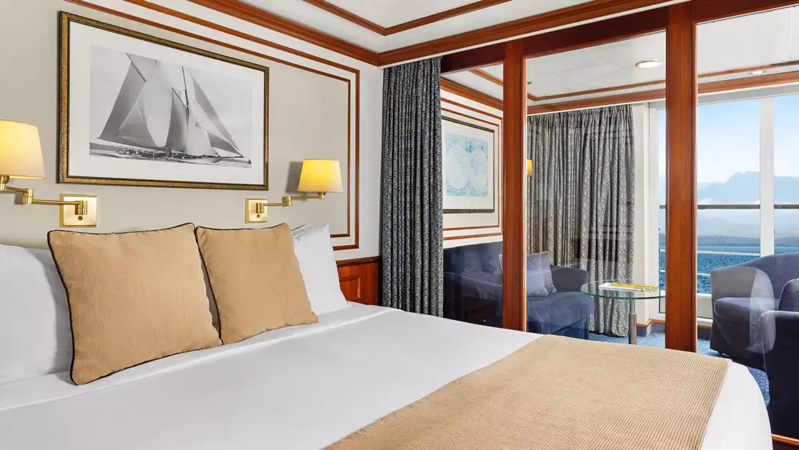 Category 6 cabin on Nat Geo Orion ship with double bed in white & beige, glass wall to seating area & private balcony.