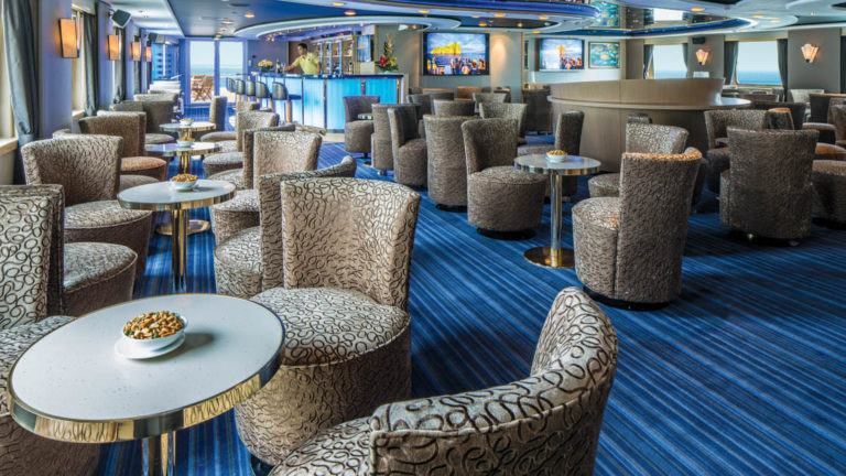Tables and chairs set up by the windows with bar in background of lounge aboard National Geographic Orion expedition ship