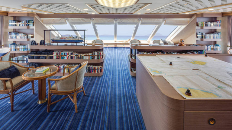 Observation lounge and library with charts on large table and seating areas aboard National Geographic Orion expedition ship