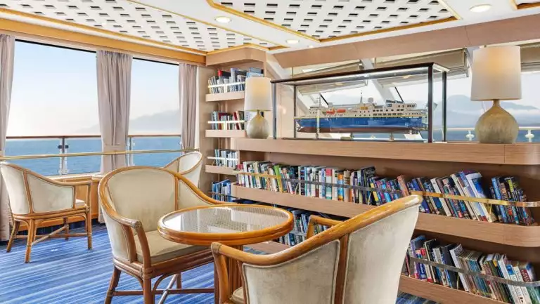 Observation lounge and library with charts on large table and seating areas aboard National Geographic Orion expedition ship
