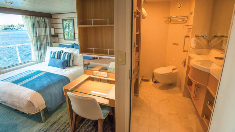 Category 5 cabin with large bed, desk, chair, large windows and bathroom with toilet, shower, sink and mirror aboard National Geographic Quest luxury expedition ship