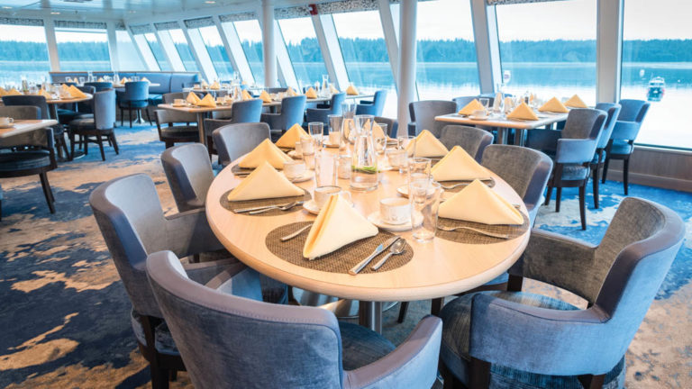 Dining room with elegant table setting and window-lined walls aboard National Geographic Quest luxury expedition ship
