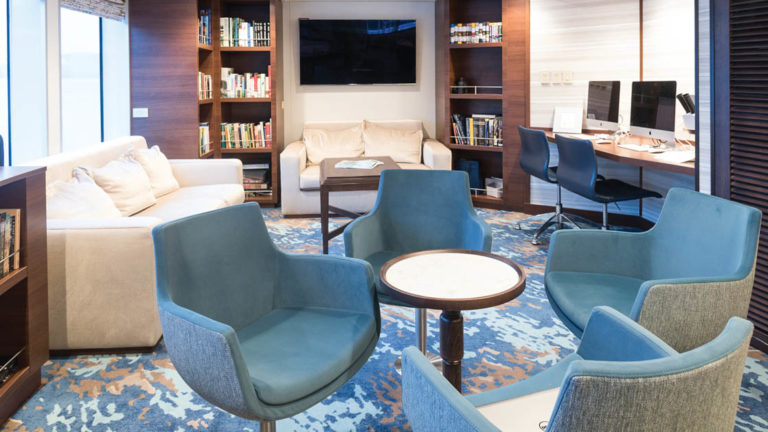 Library with couches, tables, chairs, book cases, desk with computers and TV aboard National Geographic Quest luxury expedition ship