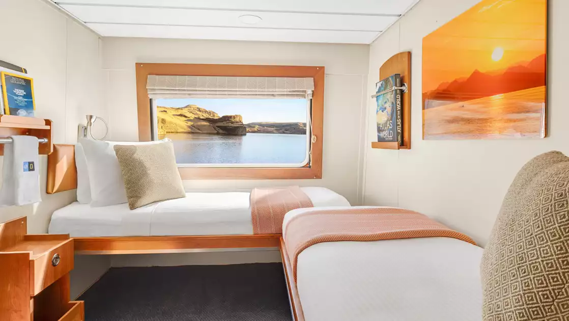 2 twin beds, nightstand & large window in cabin aboard National Geographic Sea Bird & Sea Lion expedition ships.