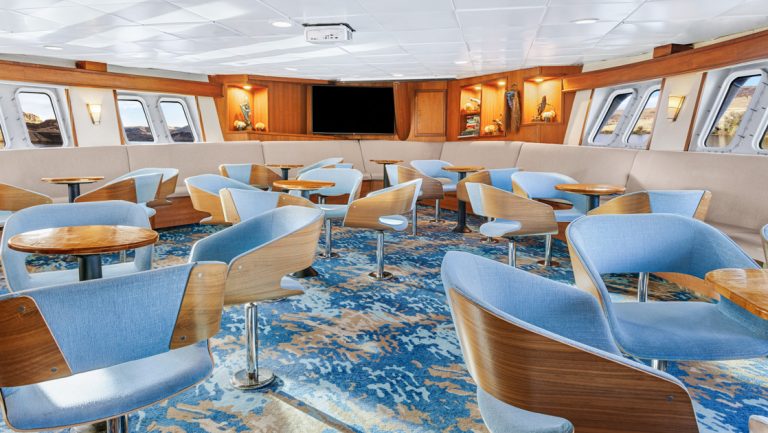 Tables and chairs near bar in window-lined lounge aboard National Geographic Sea Bird expedition ship.