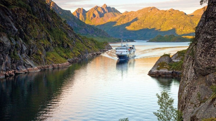 sunset casts long shadows on mountain as small cruise ship explores arctic waters