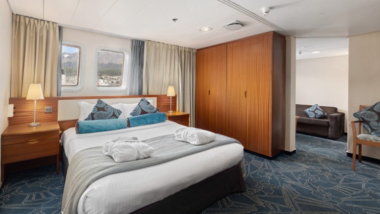 Owner's Suite on Ocean Endeavour with double bed. armoire, separate living room, windows & 2 bedside tables.