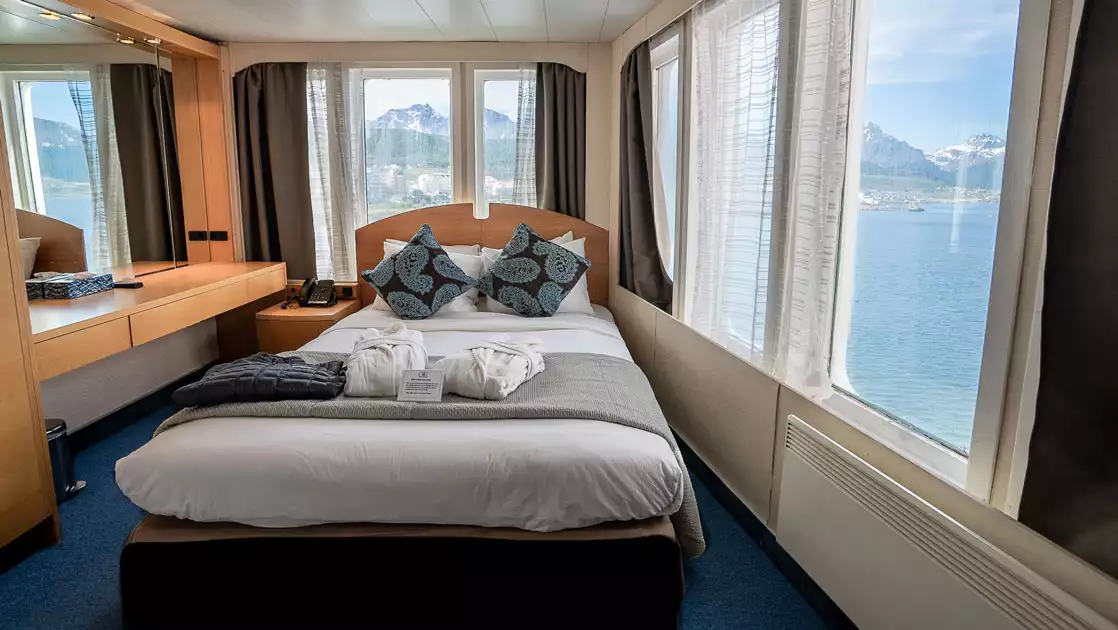 Category 5A single window cabin on Ocean Endeavour ship with double bed, 2 walls of view windows, wood armoire & desk.
