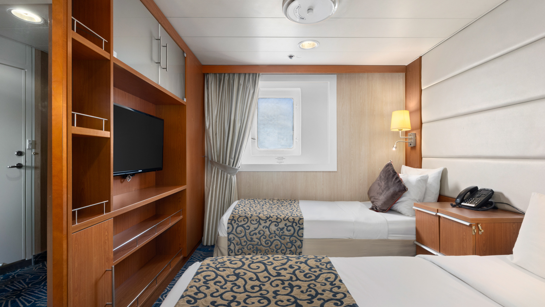 Category 7 cabin on Ocean Endeavour with window, 2 bedside tables & 2 twin beds partitioned from door by wood shelves & inset tv.