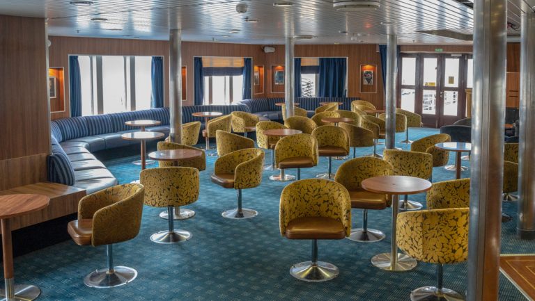 a lounge room with blue carpet and green chairs aboard Ocean Endeavour small ship
