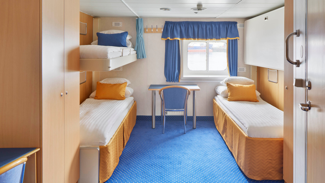 2 lower & 1 upper twin bed in white linens in triple cabin with blue & gold accents, small desk & armoire on Ocean Nova ship.