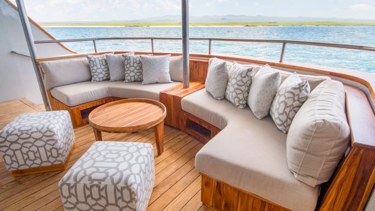 origin, theory & evolve galapagos luxury yacht sundeck with a couch and comfortable looking ottomans looking out at the ocean.
