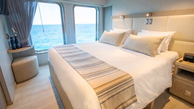 theory luxury small ship cabin with king bed and large window looking out at the ocean.