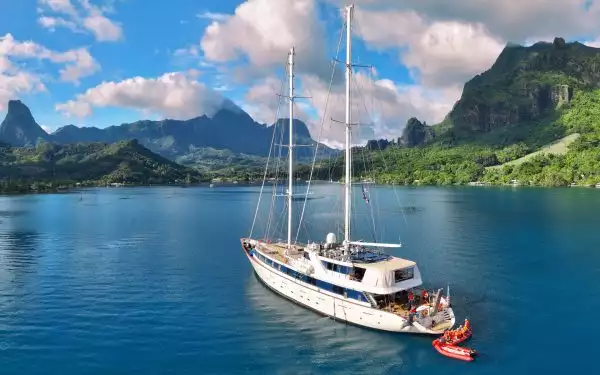 A beautiful white sailboat cruising through Tahiti with blue waters and green grass & cloudy blue skys