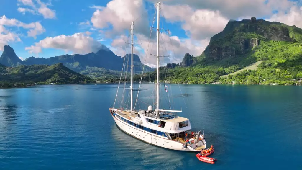 A beautiful white sailboat cruising through Tahiti with blue waters and green grass & cloudy blue skys