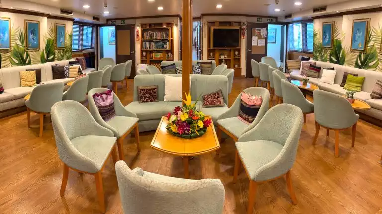 Main lounge in small ship cruise with green dining chairs and wood accents for style