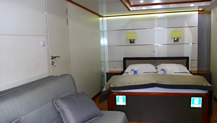 a large bed and sofa in a muted-tone room aboard the prestige luxury yacht in the mediterranean