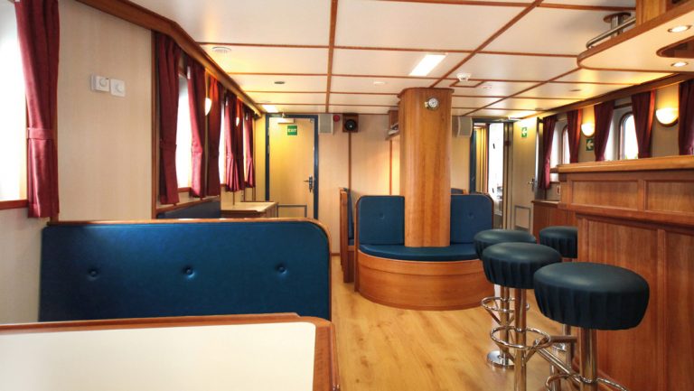 Rembrandt van Rijn small ship bar sitting area with a blue bench, bar stools, small booth table & wooden furniture