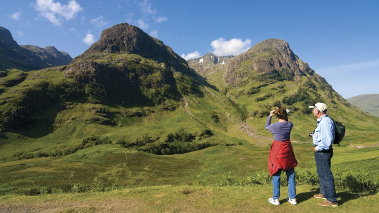 Man and woman admiring the view and taking a picture of the green mountains in Scotland