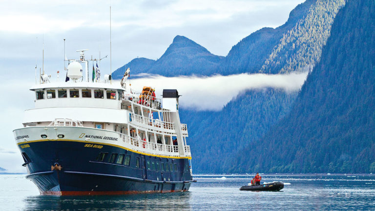 The National Geographic Sea Bird small expedition ship in the misty fjords of Alaska with a small inflatable skiff next to it.
