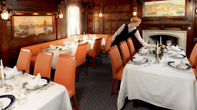 A beautiful dining room featuring rich paneling and paintings all the touches of a fine dining experience aboard the Sea Cloud Lindblad