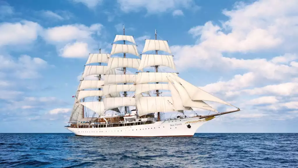 Sea Cloud: Lindblad luxury yacht with historic windjammer style & white-painted wooden hull cruising in full sail on blue sea.