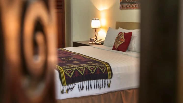 A peek into a room at Toraja Misilliana Hotel with a queen bed and colorful woven bed throw on white bed.