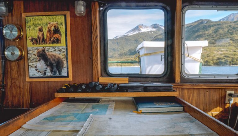 Bridge on Ursus ship in Alaska with nautical maps, binoculars, view windows & bear photos hung on wood-paneled walls.