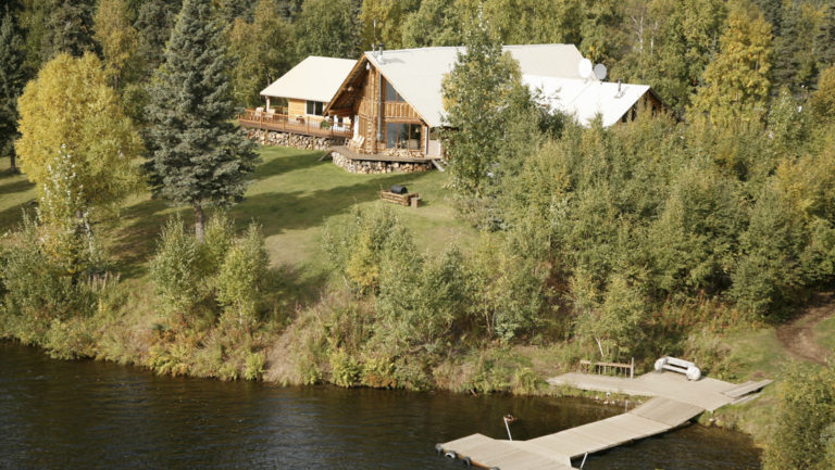 An aerial view of the Winterlake Lodge, located next to the water and situated in the Alaskan forest, with a private dock.