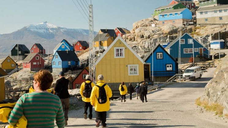 people walk down a street toward colorful houses on a bluff in greenland