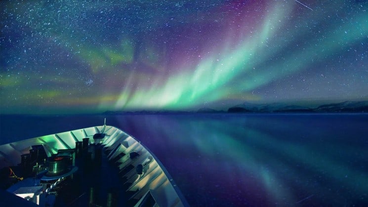 Green and purple northern lights illuminate the sky and reflect in the ocean in front of the ship for the arctic sights cruise