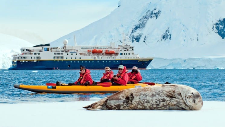 A seal lounges on the ice while a kayak full of passengers from the National Geographic voyage passes by