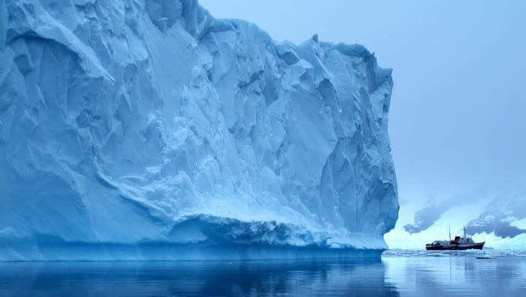 A ship cuts through sea ice next to a giant iceberg rising out of the ocean in antarctica