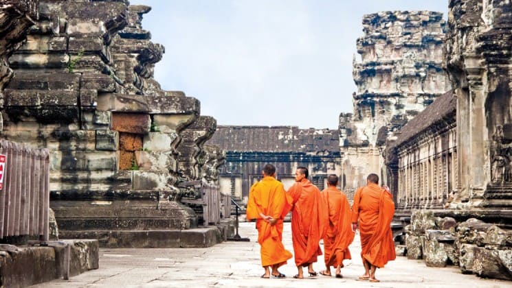 Four monks in orange robes walk through ankor wat's temples, a world heritage site in Southeast Asia