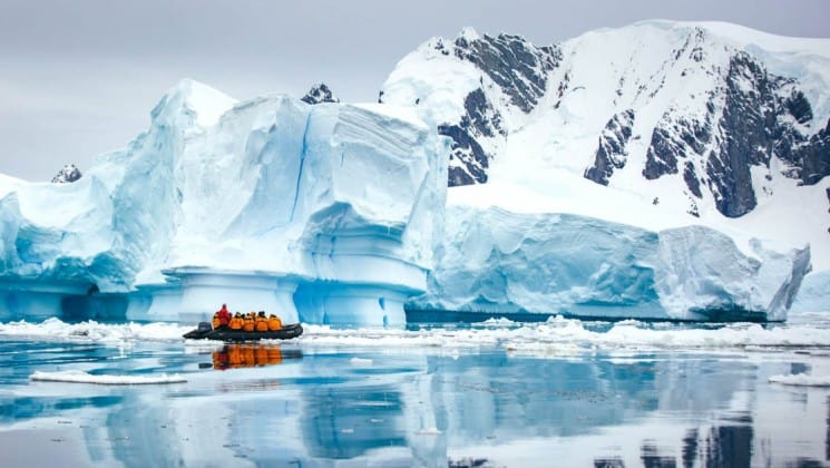 A zodiac boat with crossing the antarctic circle cruise ship carries passengers toward a gigantic iceberg floating in the ocean