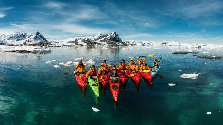 A group of sea kayaks pose in the ocean in front of icebergs in antarctica