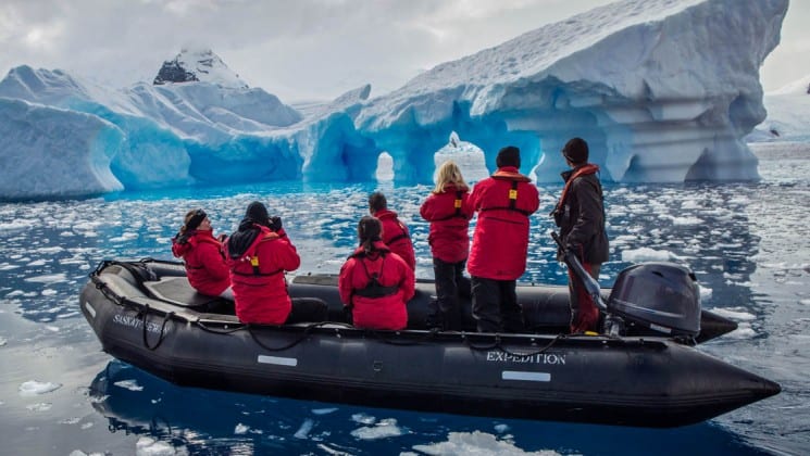 Guests from the spirit of shackleton expedition cruise sit in a zodiac with icebergs in the distance, at antarctica