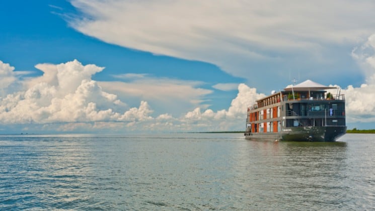 A river boat motors down the Mekong in Cambodia under a blue sky with white clouds