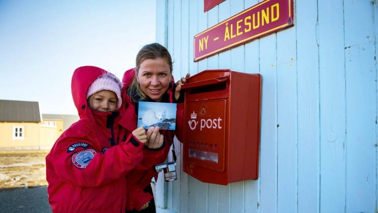 two people hold up a postcard to drop in the mail box in spitsbergen in the arctic circle