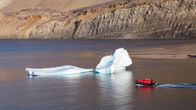 a zodiac boat motors past an iceberg near land in the arctic circle