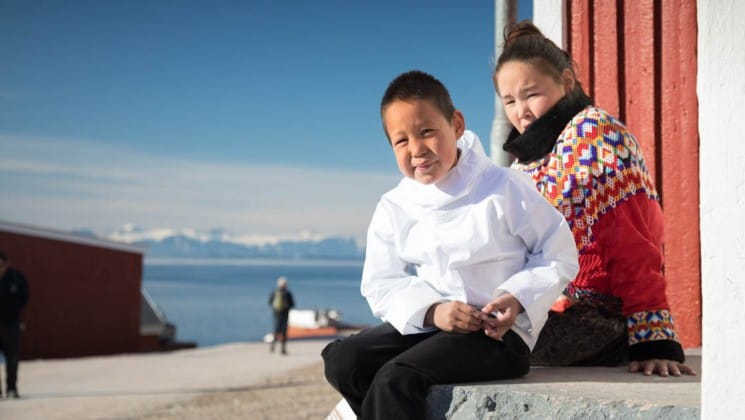 two people sit on a bench overlooking the ocean and snow-capped mountains in greenland