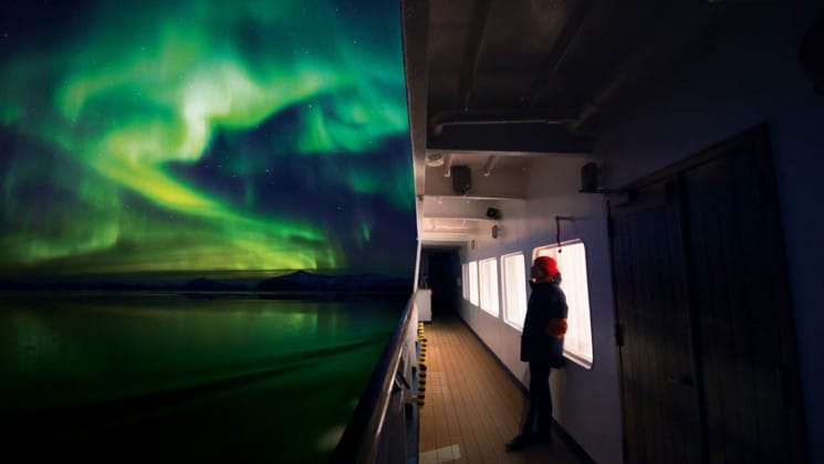 Green and blue northern lights illuminate the sky and the ocean just off the side of the ship for the arctic sights cruise
